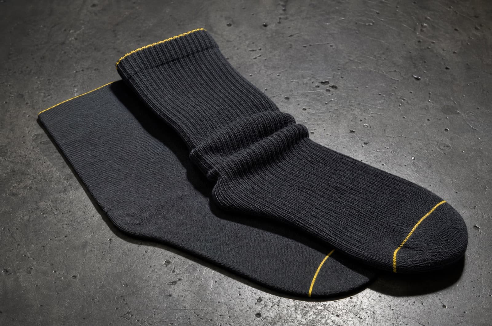 A thin liner sock and a thicker outer sock overlapping on a workbench to show the difference in thickness